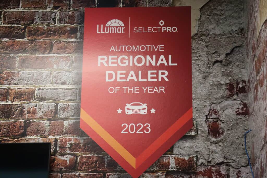 a red Commercial Sign for Best llumar window tinting printed by precision window tinting for Regional Dealer 2023 award. Sign is mounted on a distressed brick wall.